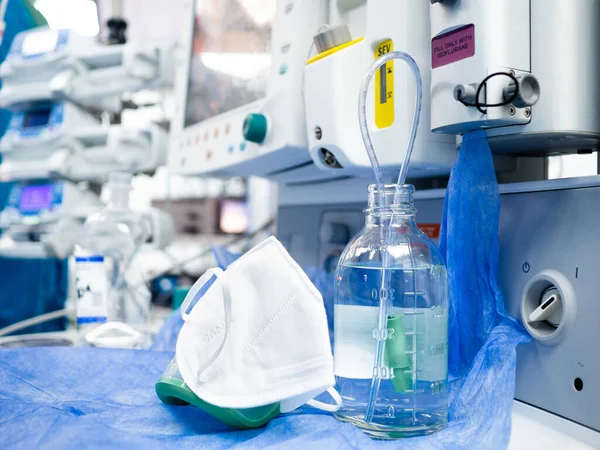 Eine Glasflasche mit Kochsalzlösung und eine weiße medizinische Maske auf dem Tisch im Krankenhaus. Stockfoto