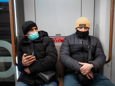 Koruyucu kıyafetli bir yolcu metro vagonunda duruyor..