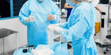 Cerrahlar birbirlerine steril ameliyat eldivenleri giymeleri için yardım ederler..