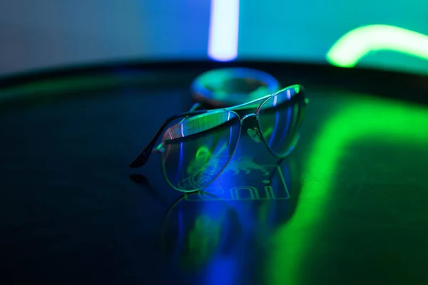 Солнцезащитные очки лежат на круглой поверхности и отражают неоновый свет — стоковое фото