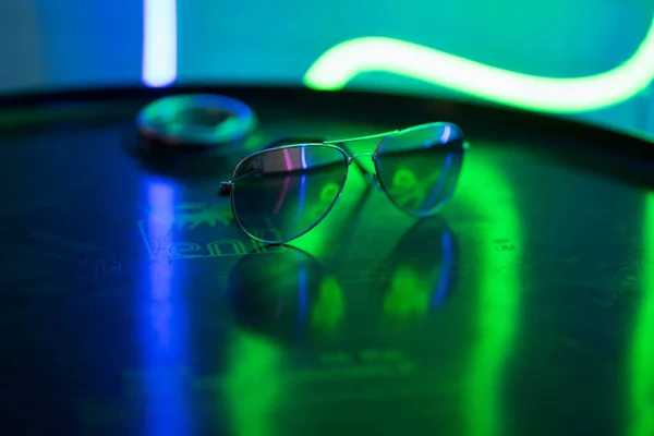 Sluneční brýle leží na kulatém povrchu a odrážejí neonové světlo — Stock fotografie