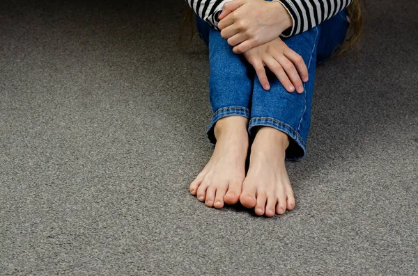 Child\'s bare feet. Girl\'s legs in jeans. Sitting on the floor.