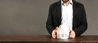 Erkek bir işadamının elinde bir evin minyatür tasarımı. Masanın üzerinde. Bir ölüye güvenlik ve koruma sağlama kavramı.