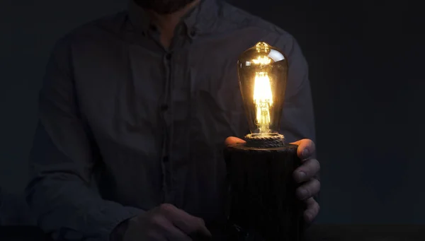 男は電球を手に持っている コンセプトアイデア テーブルランプ 木製の装飾用ランプ 暗闇の中の夜の光 — ストック写真