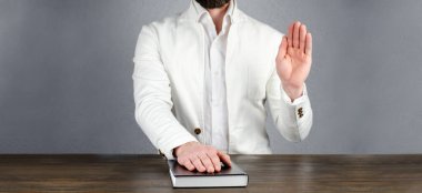 Ceketli bir adam İncil 'in üzerinde elini tutuyor. Kaldırılmış bir el ile yemin etmek. Kitabın üzerine yemin et. Söz ve Mutabakat. Yemin ederim.