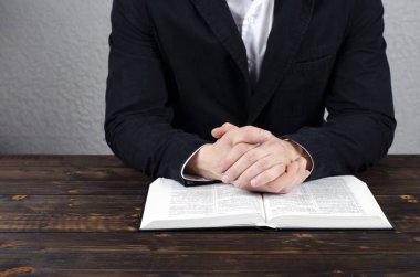 İncil 'i aç, tahta bir masanın üzerinde. Dua eden eller. Dua et. Elleri bağlı dua eden bir adam. Kutsal İncil. Masaüstü.