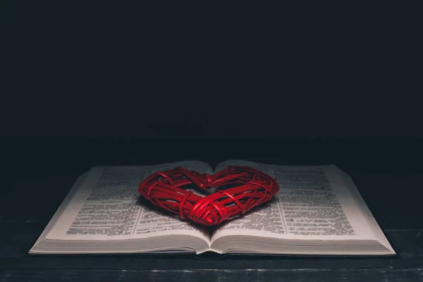 Open Bible. Red heart on the book. Holy Bible. On a black background.