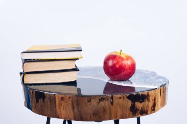 Bir yığın kitap. Masanın üzerinde bir kitap ve bir elma. Epoksi reçineden yapılmış bir masa. Mobilya.