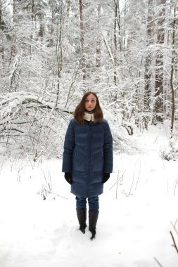 Uzun saçlı, mavi gözlü, güzel kış ormanlarında kar altında ağaçların arasında yürüyen genç ve çekici bir kadın.