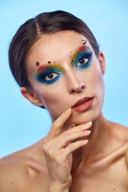 Moda yaratıcı makyaj. Temiz ve parlak ciltli genç bir kadının güzel portresi ve parlak mavi bir arka planda duran yapay elmaslarla süslenmiş.