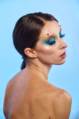 Moda yaratıcı makyaj. Temiz ve parlak ciltli genç bir kadının güzel portresi ve parlak mavi bir arka planda duran yapay elmaslarla süslenmiş.