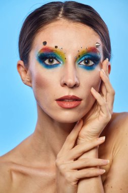 Moda yaratıcı makyaj. Temiz ve parlak ciltli genç bir kadının güzel portresi ve parlak mavi bir arka planda duran yapay elmaslarla süslenmiş.