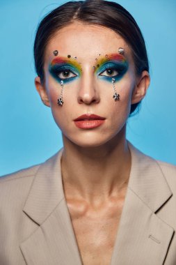 Moda yaratıcı makyaj. Temiz ve parlak ciltli genç bir kadının güzel portresi ve parlak mavi bir arka planda duran yapay elmaslarla süslenmiş.