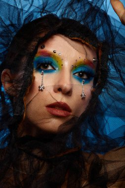 Moda yaratıcı makyaj. Temiz ve parlak ciltli genç bir kadının güzel portresi ve parlak mavi bir arka planda duran yapay elmaslarla süslenmiş.