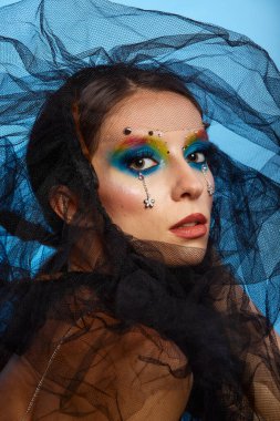 Moda yaratıcı makyaj. Temiz ve parlak ciltli genç bir kadının güzel portresi ve parlak mavi bir arka planda duran yapay elmaslarla süslenmiş.