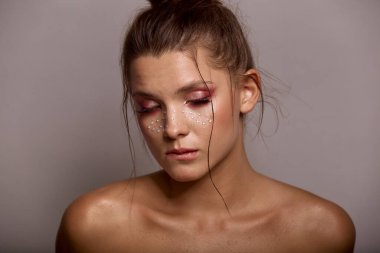 Moda yaratıcı makyajlı genç bir kadın yüzü. Temiz bir cilt ve parlak makyajla yüzünde gri bir arka planda duran çillerle.