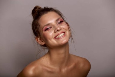 Moda yaratıcı makyajlı genç bir kadın yüzü. Temiz bir cilt ve parlak makyajla yüzünde gri bir arka planda duran çillerle.