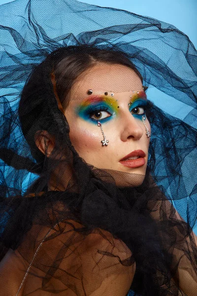 Moda yaratıcı makyaj. Temiz ve parlak ciltli genç bir kadının güzel portresi ve parlak mavi bir arka planda duran yapay elmaslarla süslenmiş.