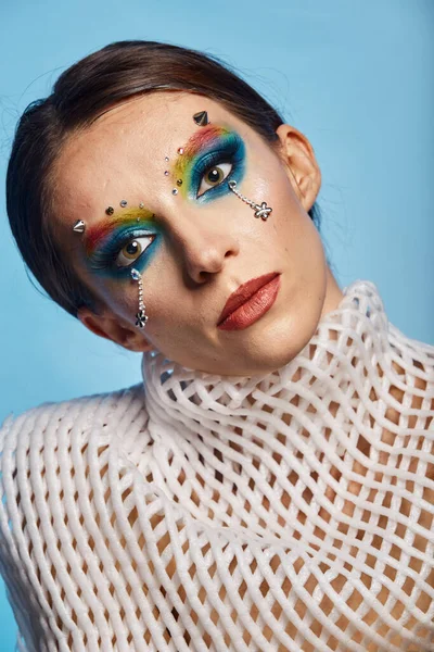 Moda yaratıcı makyaj. Temiz ve parlak ciltli genç bir kadının güzel portresi ve parlak mavi bir arka planda duran yapay elmaslarla süslenmiş.