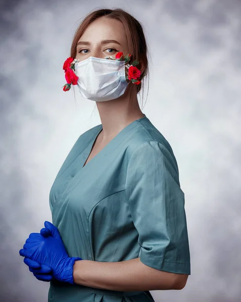 Portrait young confident woman doctor in medical face mask with fresh and lively flowers, wearing uniform and latex medical gloves. Spring allergy, COVID-19 protection, fresh breath concept