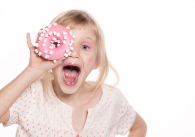 Küçük mutlu kız, beyazın üstünde izole edilmiş çörek yiyor. Yüzük donutlu sarışın bir çocuk. Mutlu çocuklar günü ve tatlı bir hayat. Metin için boş alan