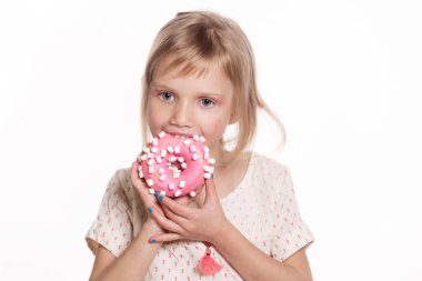 Küçük mutlu kız, beyazın üstünde izole edilmiş çörek yiyor. Yüzük donutlu sarışın bir çocuk. Mutlu çocuklar günü ve tatlı bir hayat. Metin için boş alan
