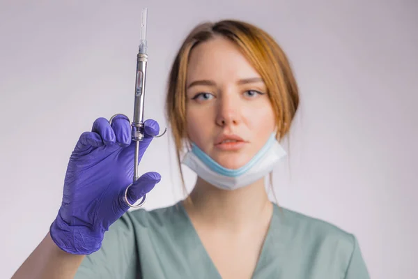 注射器を持つ魅力的な女性歯科医の肖像 灰色の背景に均一な医療面マスクとラテックス医療手袋を身に着けています — ストック写真