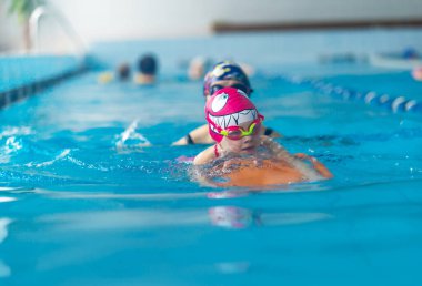 Anne ya da koç portresi halka açık yüzme havuzunda kanat çırpan küçük bir kızla yüzmeyi öğreniyor. Metin için boşluk