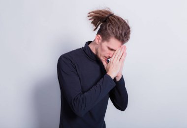 Dua eden ya da soran elleri kapalı özür diler. Koyu gri balıkçı yaka kazaklı ve kafasında kısa rastalı gri arka plan fotokopi alanı olan adam.