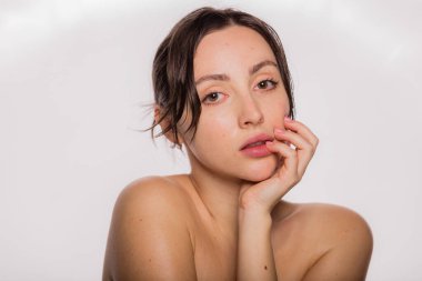 Temiz tenli, gülümseyen ve yüzüne dokunan genç bir kadının güzel yüzü. Beyaz arkaplanda duran esmerin güzel portresi