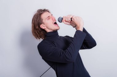 Duygusal portresi sallanan komik adam mikrofona şarkı söylüyor, arka plandaki gri fotokopi alanından izole edilmiş.