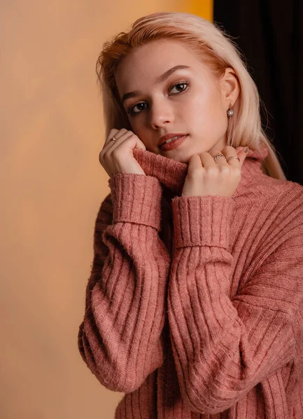 Seductive woman posing provocatively in warm sweater and sexy pink lingerie. Sporty figure on a half black and orange gray background. Slim woman in sexy erotic underwear warm tone.