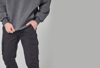 Koyu gri kazaklı ve siyah pantolonlu bir adam. Gri arka planda duruyor. Yazdırma ya da dizayn şablonu için bir model. Temel giyim tarzı. Logo yok.