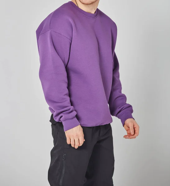 Cropped shot of man in purple blank sweatshirt and black pants. Standing on gray background. Mockup for print or design template. Basic clothing line no logo