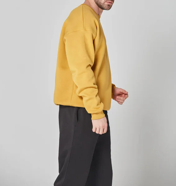 Cropped shot of man in yellow blank sweatshirt and black pants. Standing on gray background. Mockup for print or design template. Basic clothing line no logo