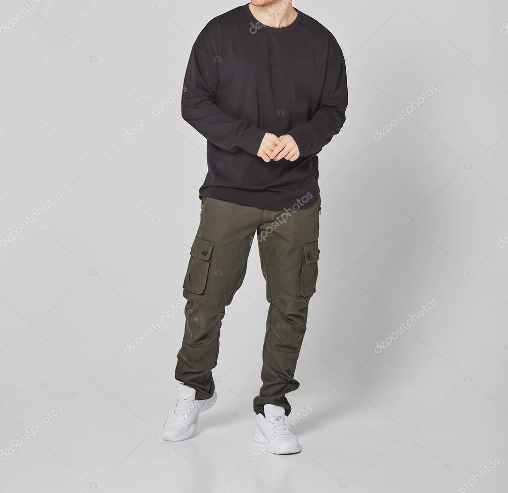 Cropped shot of man in black blank long sleeved and green cargo pants. Standing on gray background. Mockup for print or design template. Basic clothing line no logo