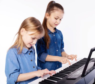 Müzik dersi. Müzik okulundaki iki kız çocuğu beyaz arka planda piyano çalmayı öğreniyor.