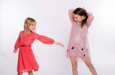 Playful kids, funtime concept. Portrait of cute two girls 6-8 years old wearing pink dress and dancing isolated on white background. Mother's Day, love family, parenthood childhood concept clipart