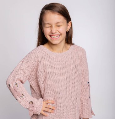 Gülümseyen mutlu bir kız çocuğunun portresi. Gri arka planda pembe süveter giyen 8 yaşında tatlı bir kız yüzü.