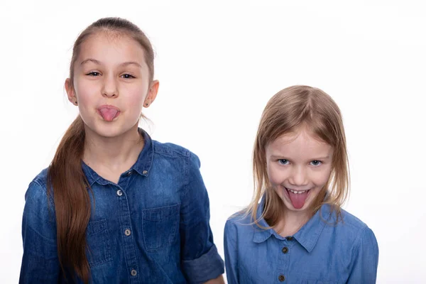 2人の子供の女の子6と8広い口を開いて 舌と優雅さを示しています 白い背景の上にデニムのドレスの顔の式を身に着けている子供 — ストック写真