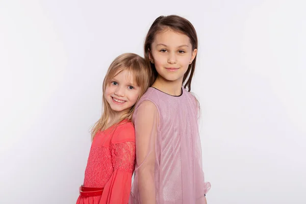 2人のスタイリッシュな友人や姉妹の子供の女の子はお互いに背を向けて立っています ピンクのドレスを着て白い背景に隔離された背中に立っている女の子 — ストック写真