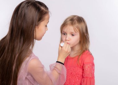 İki kız arkadaş ya da kız kardeş dudaklarına ruj sürüyor. Tatile hazırlanmak için birbirimize makyaj yapmada yardım ediyoruz. Birlikte beyaz arka planda izole edilmiş eğleniyoruz.