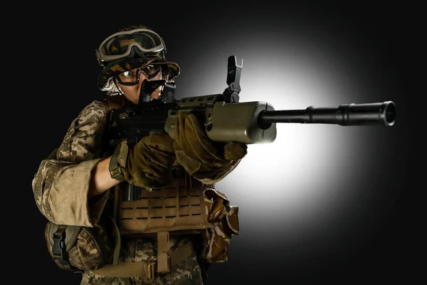 Woman army soldier in combat uniforms with assault rifle, plate carrier, goggles and backpack. Studio shot, dark background