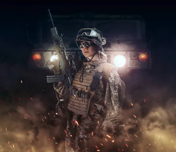 Woman army soldier in combat uniforms with assault rifle, plate carrier, goggles and backpack. Studio shot in smoke, dark background