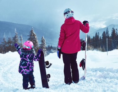 Birlikte kayak yapan anne ve kızın arka görüntüsü ya da güneşli kış günlerinde kayak merkezine gitmenin yeni bir yolu, seyahat tatili, manzara dağları arka planı..