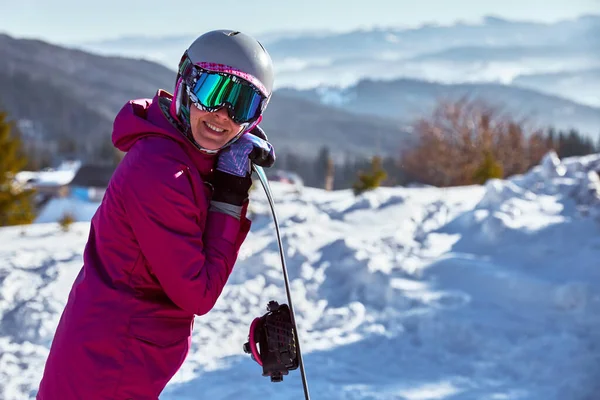 带着装备头盔和护目镜的妇女滑雪者手持雪板 在阳光下躺在滑雪场顶上 山顶是阳光明媚的冬日喀尔巴阡山 乌克兰 给你留个空白处 — 图库照片