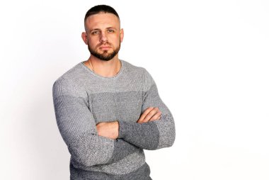 Gri örgü süveterli arkadaş canlısı genç adam ellerini göğsüne çapraz yapıyor. Boşluk beyaz arkaplanı kopyala Sonbahar-kış kıyafet koleksiyonu