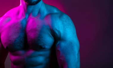 Sportif vücut geliştiren adam renkli neon ışıkta çıplak kas gövdesiyle poz veriyor. Neon stüdyo ışıklarında göğüs ve karın kasları görünüyor..
