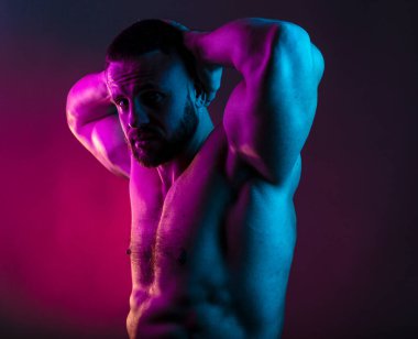 Sportif vücut geliştiren adam renkli neon ışıkta çıplak kas gövdesiyle poz veriyor. Neon stüdyo ışıklarında göğüs ve karın kasları görünüyor..