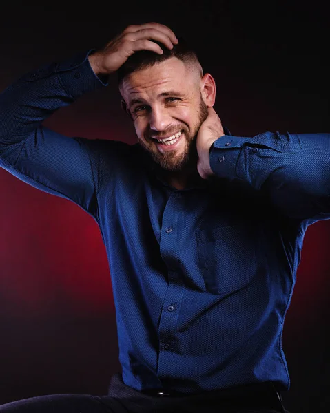 Surprised and glad man in blue shirt, hold hands on his head. Handsome Posing in studio on dark red background